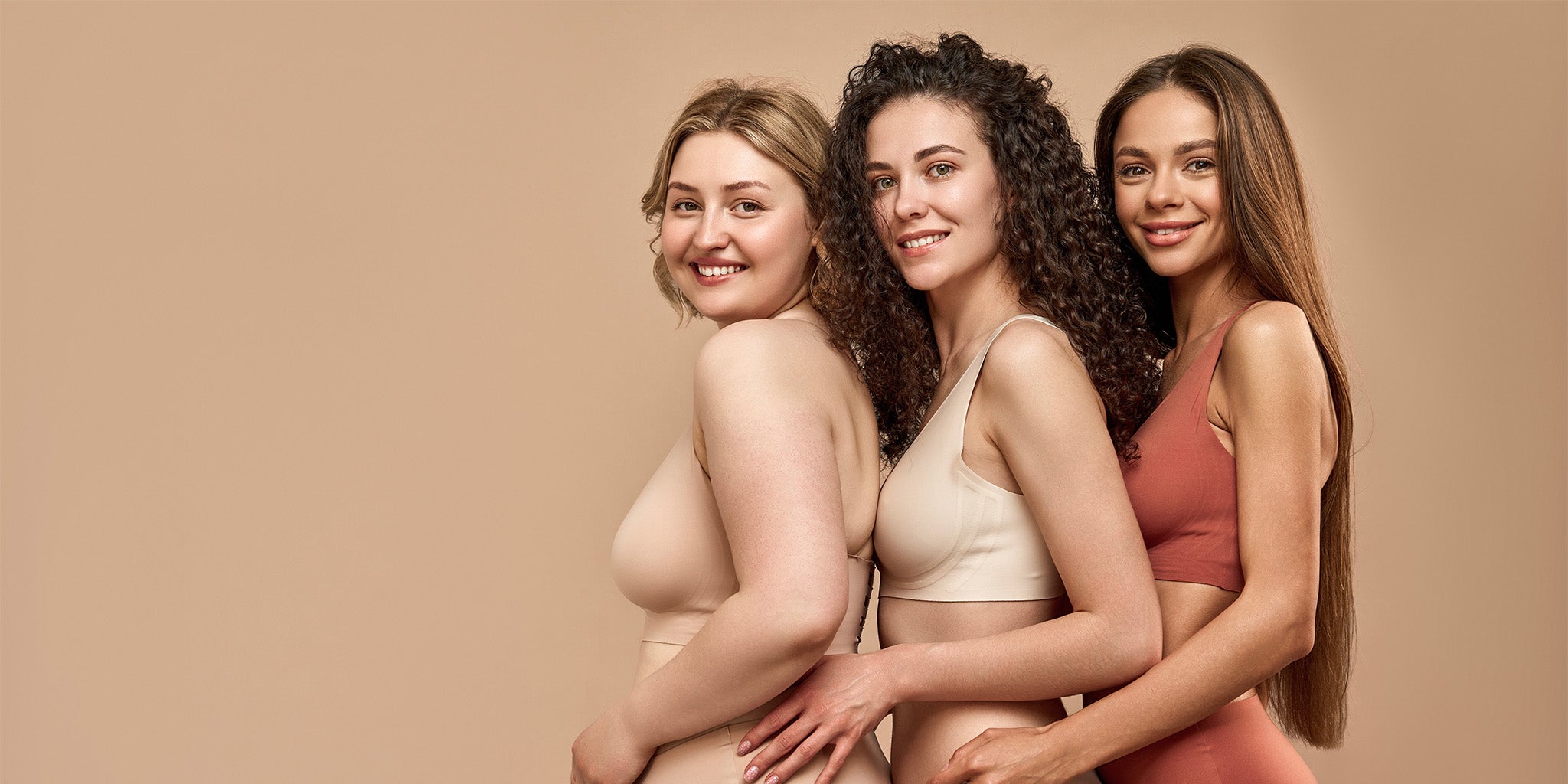 Three women, each with different body types in their underwear. They are hugging and looking at the camera.