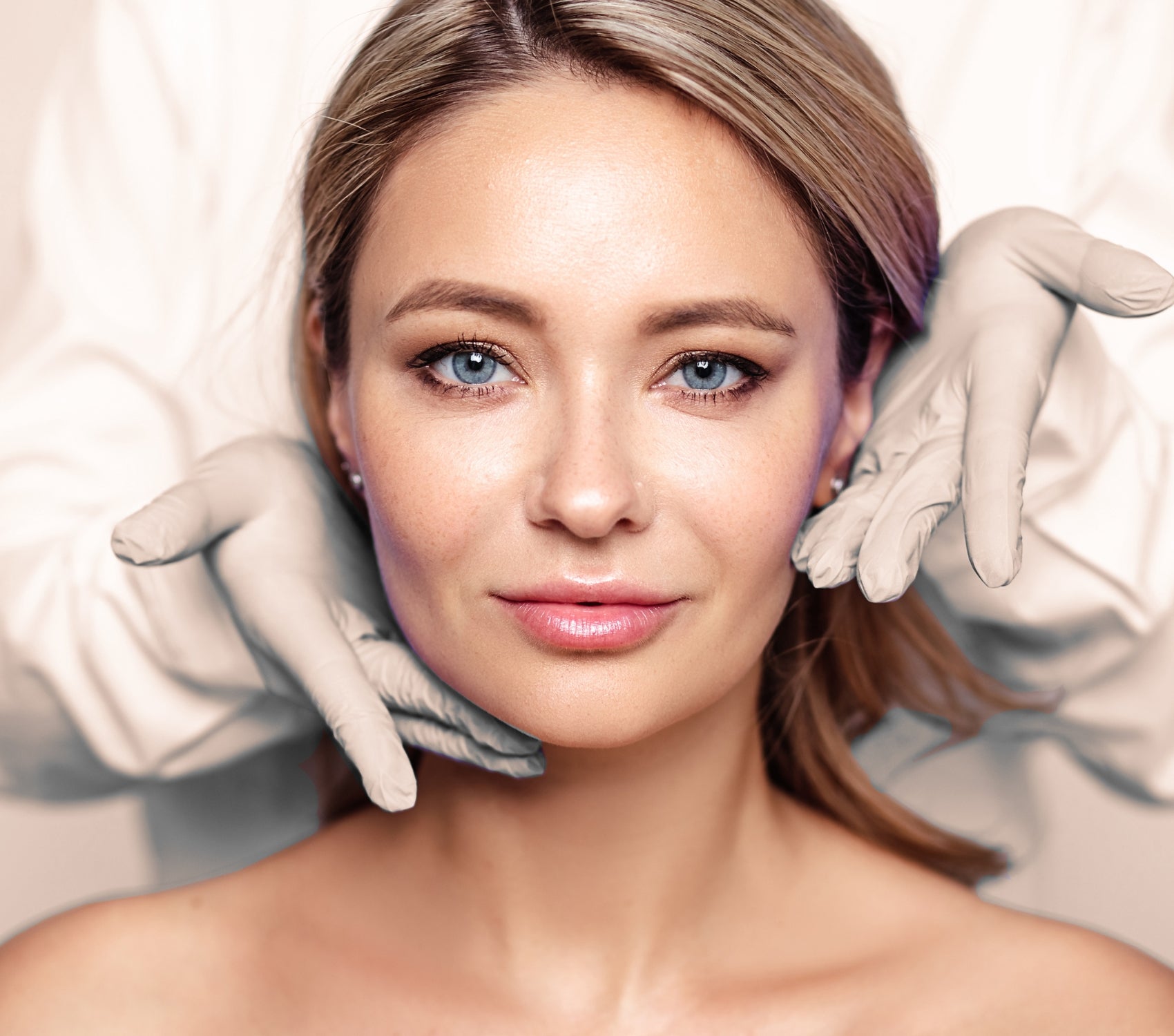 A woman looking at the camera while a pair of gloved hands hold her face. 